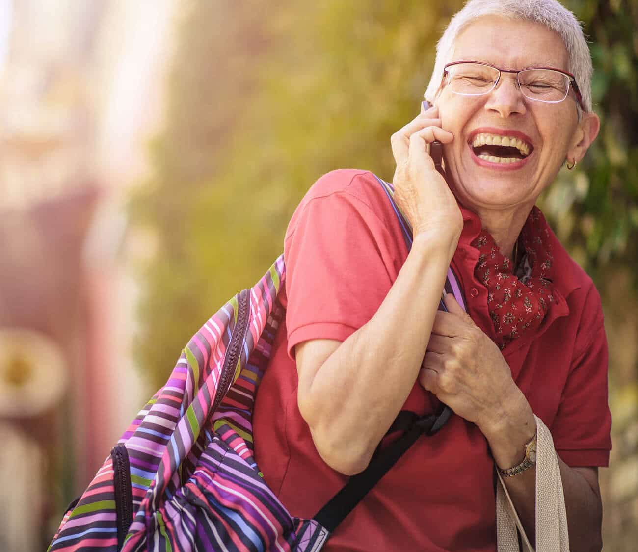 elderly woman carrying a backpack while talking on the phone and laughing