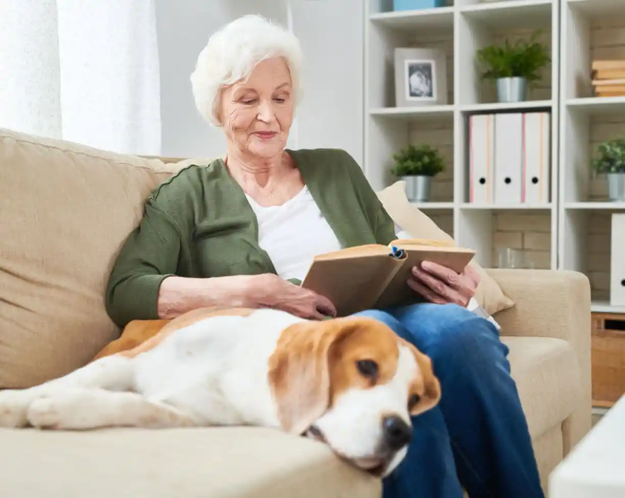 senior woman on couch reading book with dog